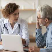 Image of female health care provider talking with older male patient, in front of a computer screen.